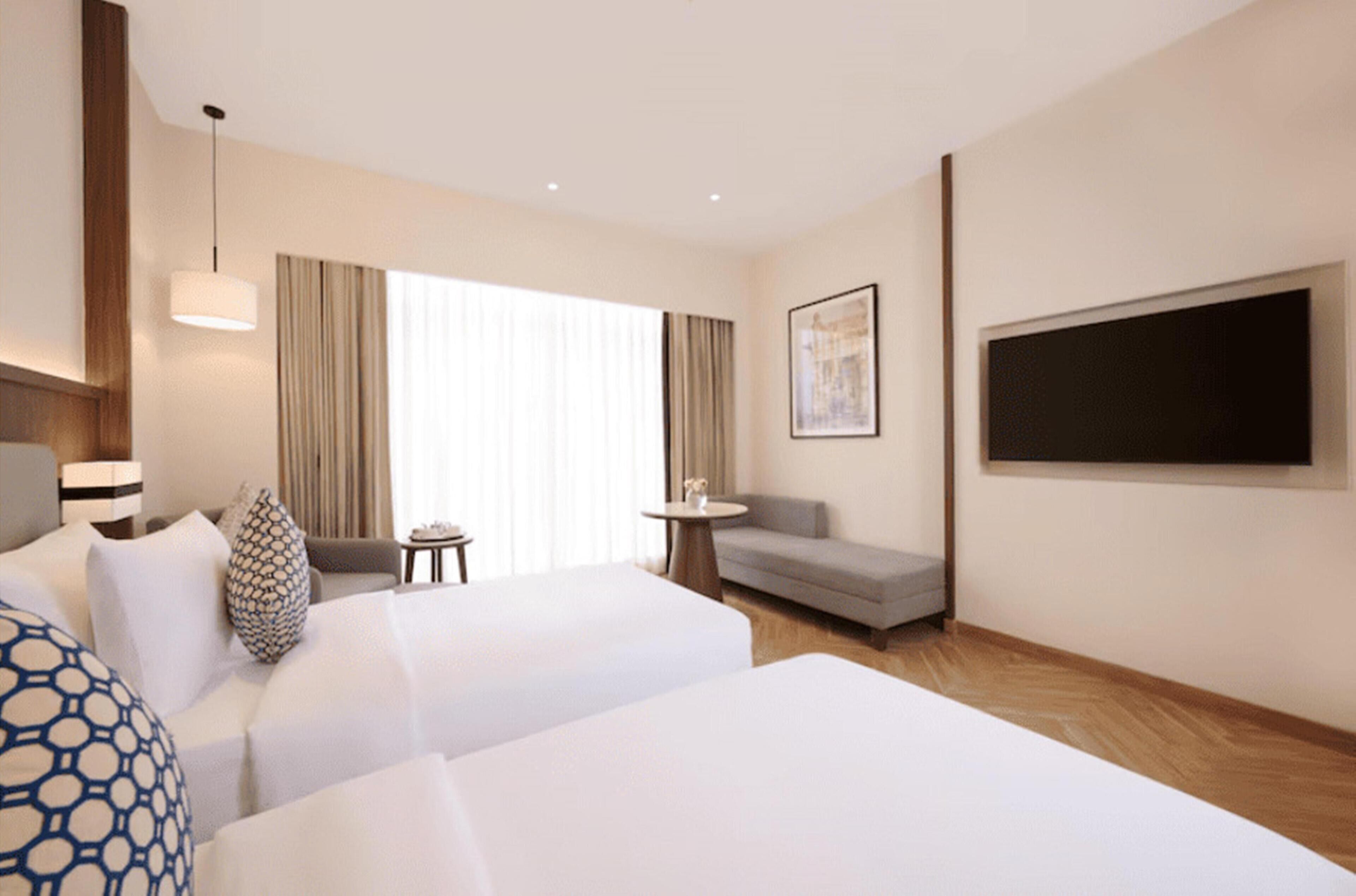 A hotel room with two beds, a sofa, a small table, a TV, and a window with curtains.