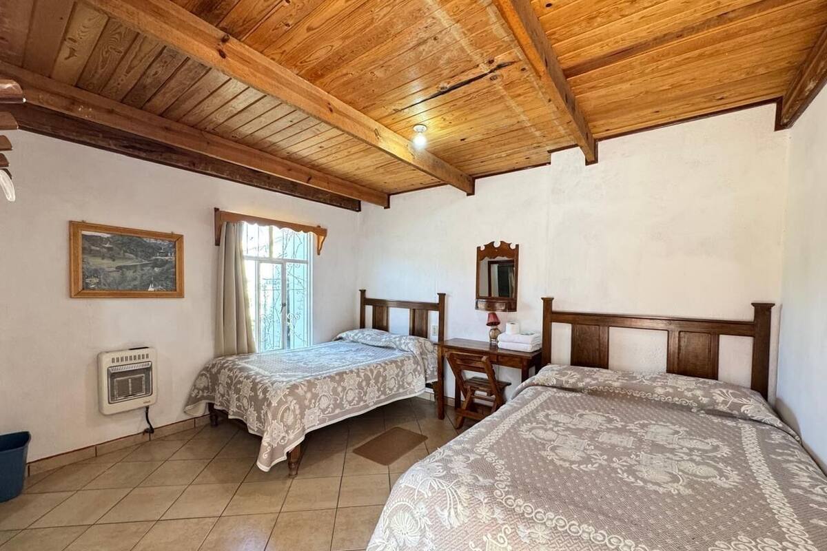 Une chambre avec deux lits, un plafond en bois, une fenêtre avec des rideaux, un bureau et un radiateur.