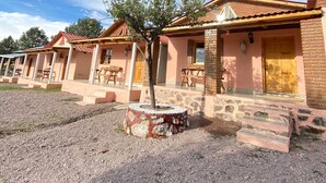 Una hilera de edificios de una planta con un camino de grava, un árbol en el centro y un cielo despejado.