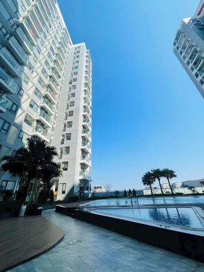 A high-rise building with balconies, a swimming pool, and palm trees. - Beer Home Apartment - Hue Free Pool (Thanh Pho Hue)