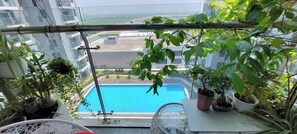 A balcony with a view of a swimming pool, potted plants, and a clear sky. - Beer Home Apartment - Hue Free Pool (Thanh Pho Hue)