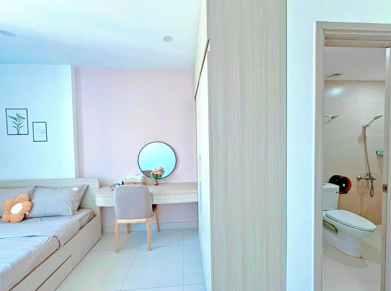 A modern bedroom with a bed, a desk, a chair, a round mirror, and a bathroom with a shower and toilet.