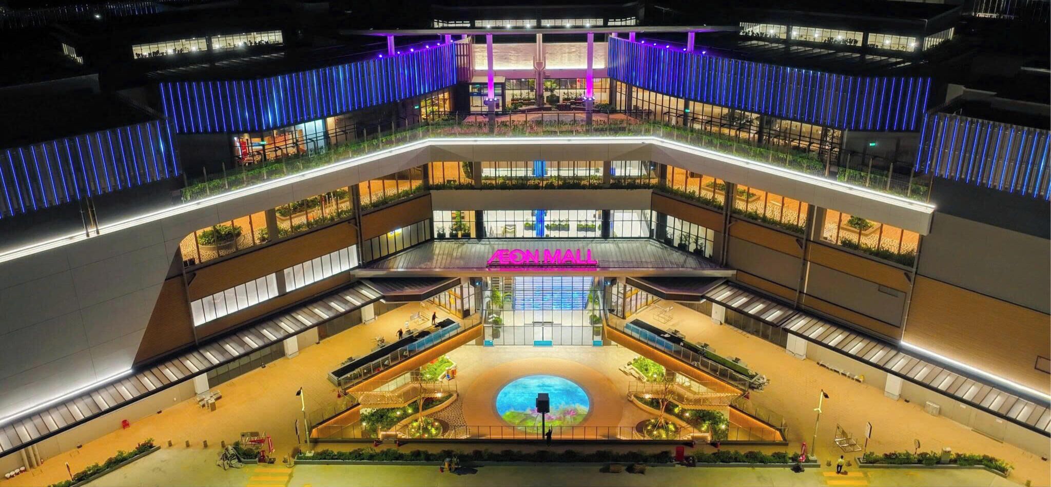 Un atrium de diversos nivells amb una estructura circular central, baranes de vidre i un cartell de neó per a AEON MALL.