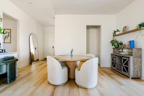 A modern dining area with a round table, two chairs, and a cabinet with glassware. - 3-Bedroom Pool House with Golf & Sunset Views (Indio)