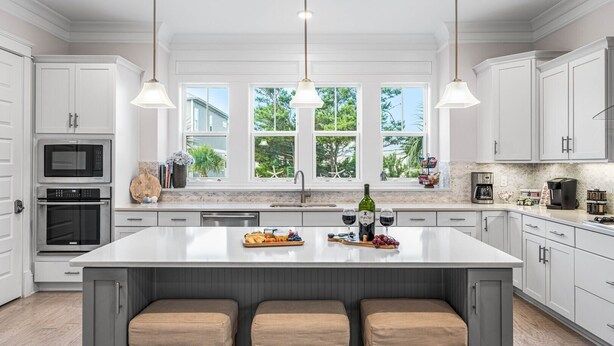 A modern kitchen with white cabinetry, a large island with stools, a built-in oven, a microwave, and a coffee maker. - Luxury Prominence Home – Pool, Beach & Golf Cart (Inlet Beach)