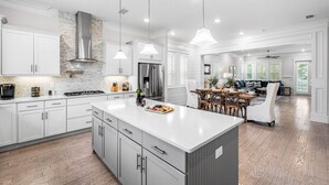 A spacious kitchen with white cabinetry, a large island, and modern appliances. - Luxury Prominence Home – Pool, Beach & Golf Cart (Inlet Beach)