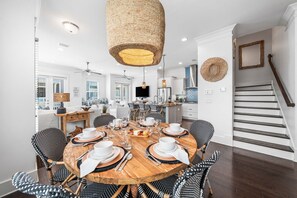 A modern kitchen with white cabinets, a wooden dining table set for six, and a staircase with dark wood steps. - 30A Coastal Therapy – Pool, Beach & Golf Cart (Inlet Beach)