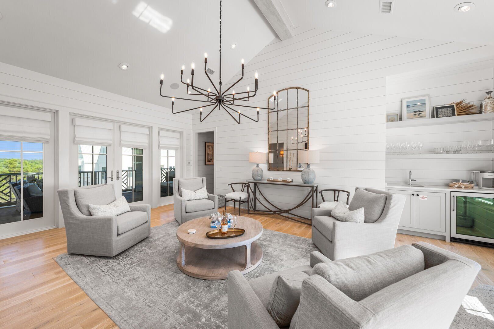 A spacious living room with a chandelier, grey sofas, a coffee table, and a kitchen area with a dining table.