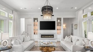 A spacious living room with a large flat-screen TV, a fireplace, and a chandelier. - Crown of 30A – Pool, Pets & Golf Cart (Santa Rosa Beach)