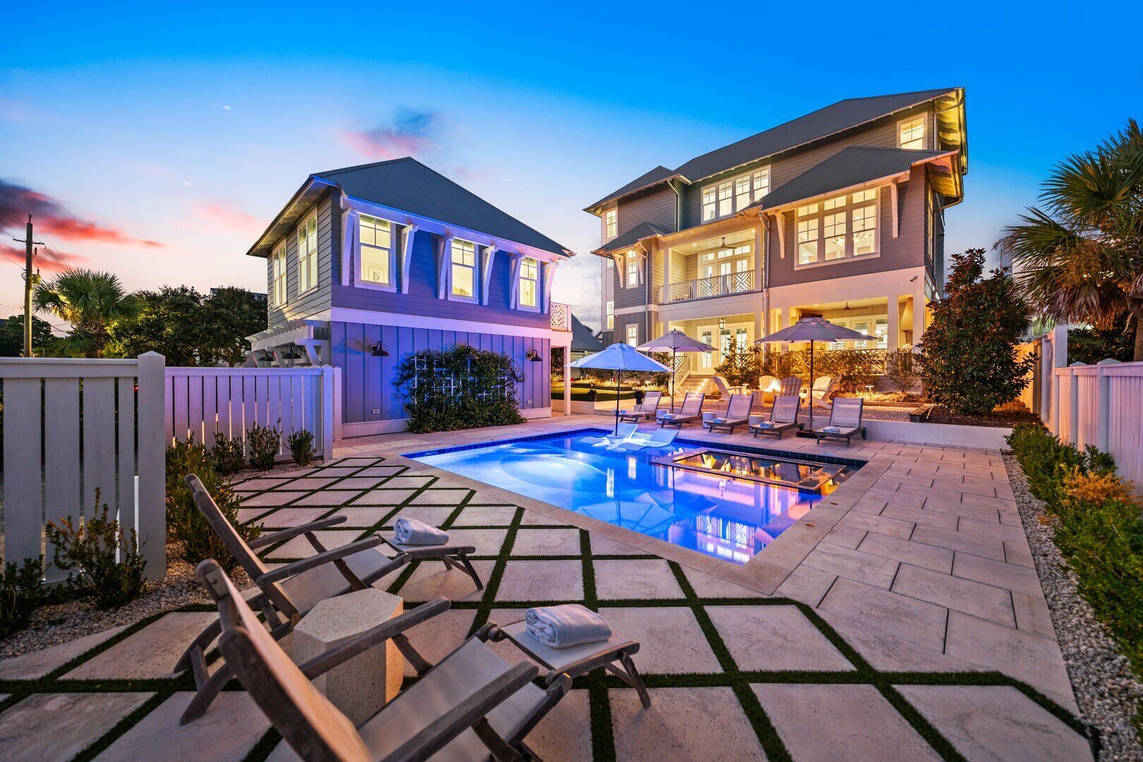 A two-story house with a swimming pool, lounge chairs, and umbrellas.