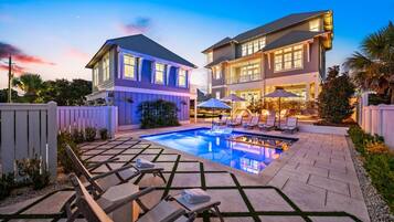 A two-story house with a swimming pool, lounge chairs, and umbrellas.