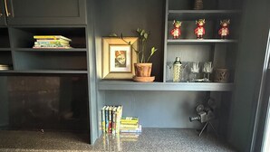 Een thuiskantoor met een donkerblauwe bureau, een groene bureaustoel en planken met boeken, een potplant en decoratieve objecten.