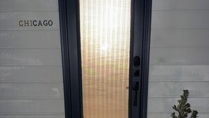 Eine dunkelblaue Tür mit einer satinierten Glasscheibe, einer Fußmatte mit der Aufschrift "goodbye hello" und einem kleinen Blumentopf daneben.