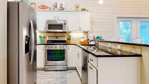 Una cucina moderna con elettrodomestici in acciaio inossidabile, mobili bianchi e pavimento in piastrelle a spina di pesce.