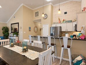 A dining area with a wooden table, white chairs, and a decorative doily. - Private Heated Pool, Pet Friendly, Golf Cart Included (Port Aransas)