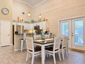 A kitchen with white cabinets, stainless steel appliances, and a dining area with white chairs and a table. - Private Heated Pool, Pet Friendly, Golf Cart Included (Port Aransas)