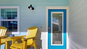 Una stanza con una porta blu, due poltrone Adirondack gialle, un tavolino e un tappetino d'ingresso decorato con illustrazioni di granchi.