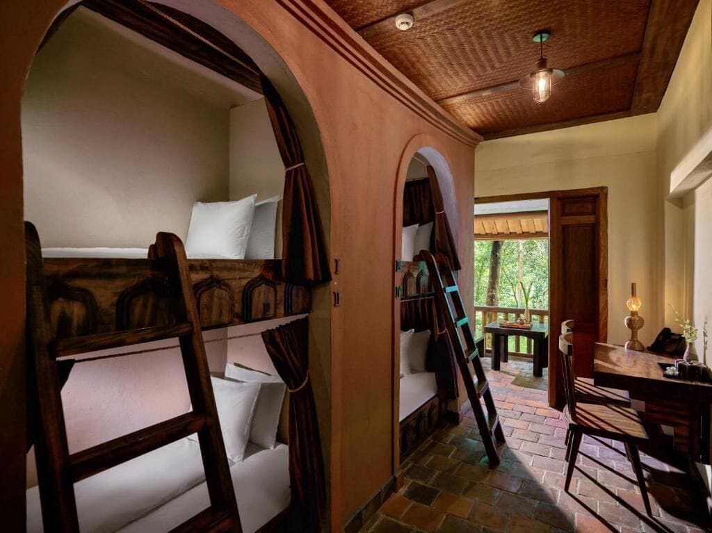 A cozy room with bunk beds, a wooden ceiling, and a stone floor.