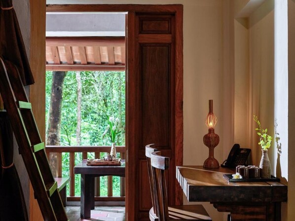 Una habitación con escritorio de madera, una silla, una lámpara y una ventana que ofrece vista a zonas verdes.