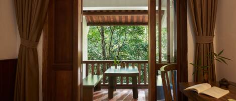 A room with a bed, a wooden desk with an open book, a bench, and a table with a plant.