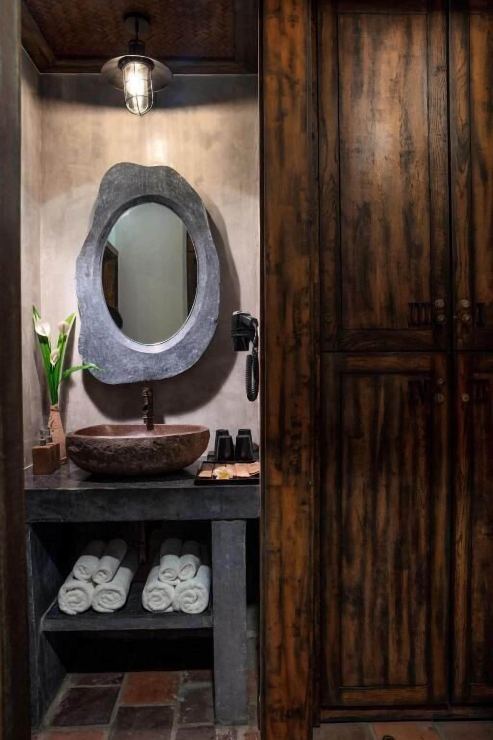 A bathroom with a round mirror, a stone sink, and a wooden door.