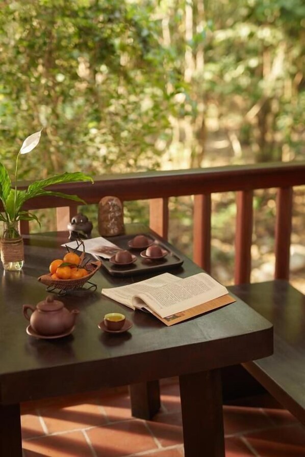 A wooden table with a book, teapot, cups, and a basket of oranges on a balcony with a view of greenery. - Yen Tu Village  (Yen Tu)