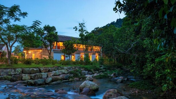 Un edificio de dos pisos con un muro de contención de piedra y un arroyo que fluye al frente.