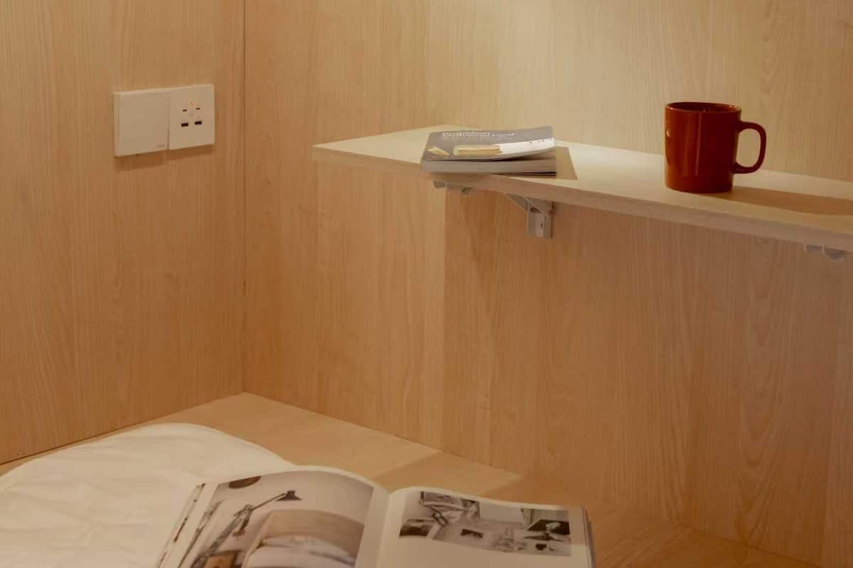 Ein Zimmer aus Holz mit einem Bett, einem Regal mit einem Buch und einer Tasse sowie einer Steckdose.