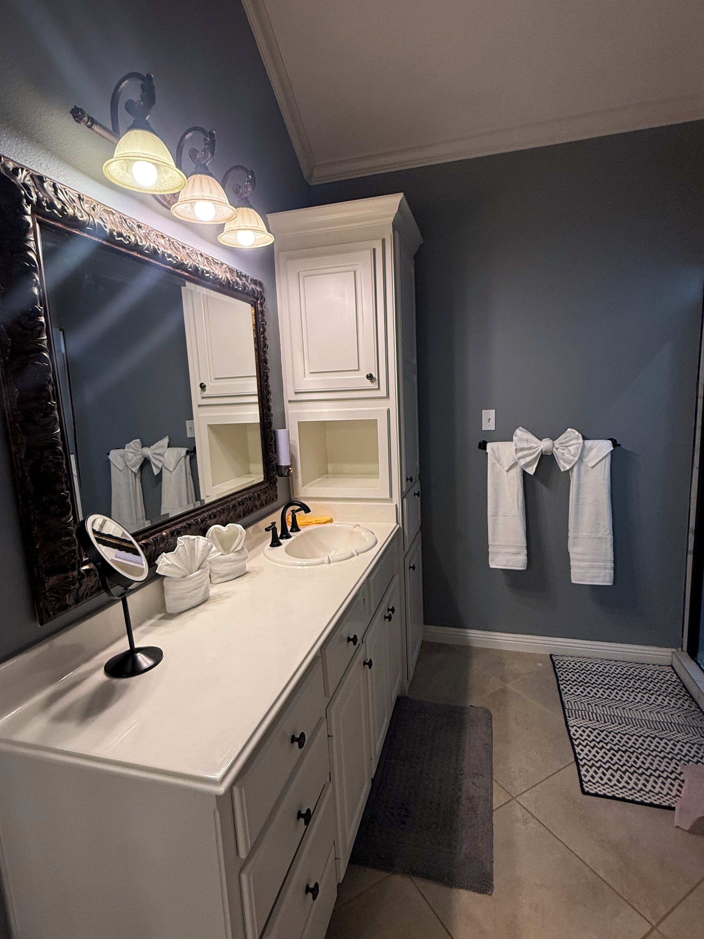 A bathroom with a white vanity, a large mirror, a sink, and a towel rack with towels.