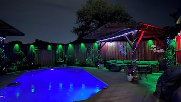 A backyard with a pool, wooden deck, and outdoor furniture.