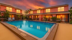 A two-story hotel with a swimming pool, palm trees, and a sunset sky. - Beautiful Townhome Near Sanibel (Fort Myers)