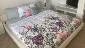 A bedroom with a floral bedspread, a television on a stand, and a nightstand with a lamp. - Beautiful Townhome Near Sanibel (Fort Myers)