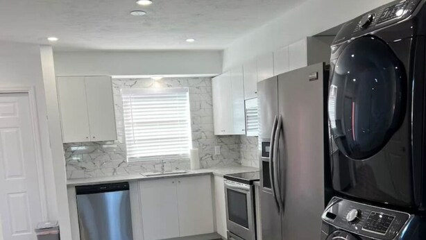 A modern kitchen with white cabinets, a stainless steel dishwasher, a built-in oven, and a black washing machine. - Beautiful Townhome Near Sanibel (Fort Myers)