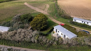 Ländliche Landschaft mit Feldern, einem großen Baum und zwei weißen Gebäuden mit grauen Dächern.