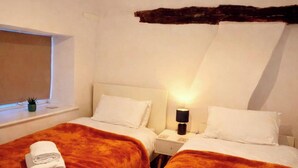 Camera d'albergo con due letti, ciascuno con una testiera bianca, una finestra vista e un piccolo tavolo con lampada.