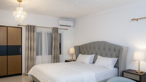 Habitación de hotel con cama, mesitas de noche, candelabro, unidad de aire acondicionado y armario.