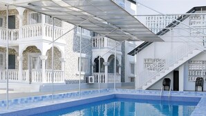 Una piscina con borde de azulejos, una zona cubierta con barandilla blanca y una escalera que lleva a un nivel superior.