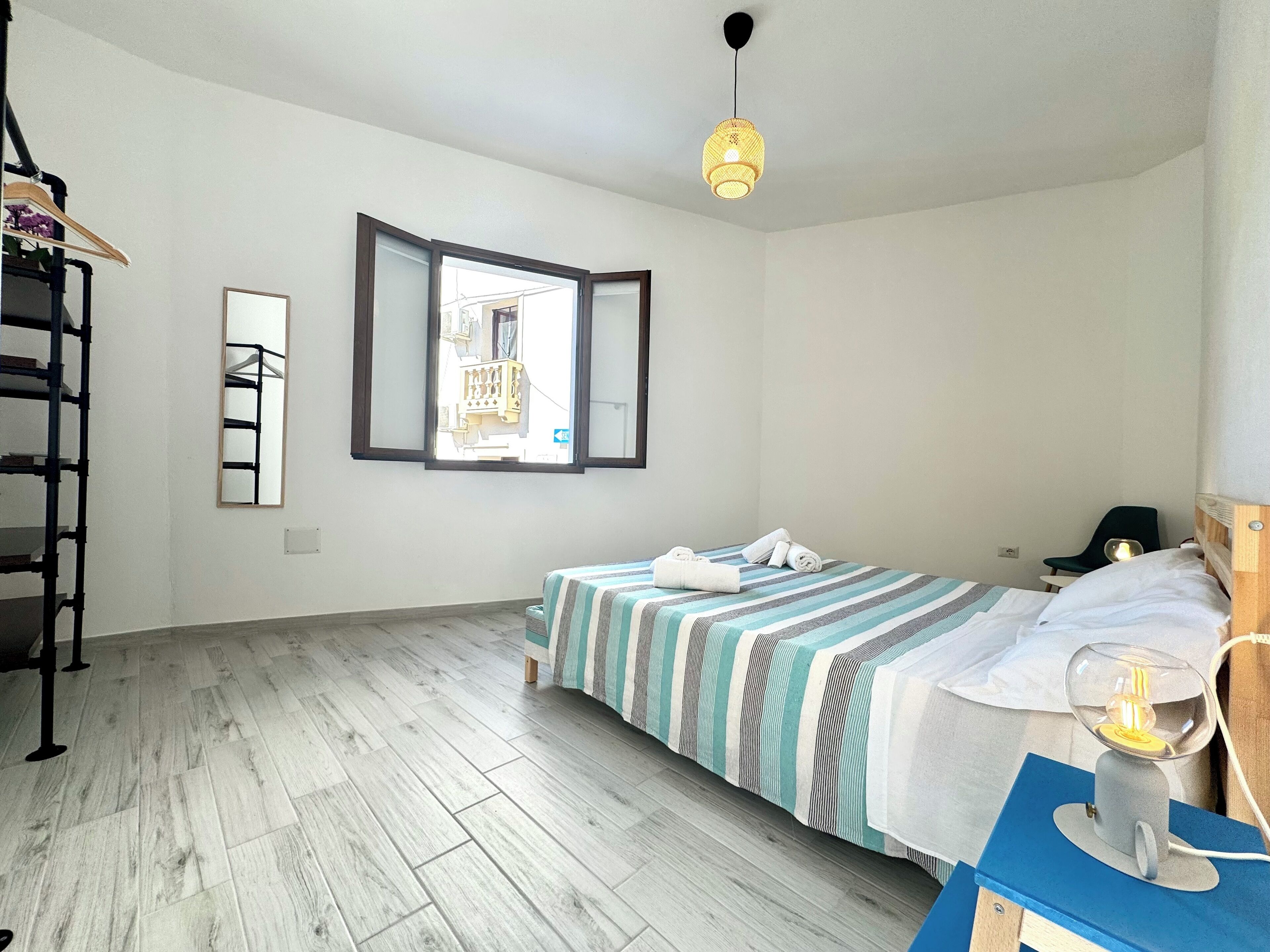 Un dormitorio con cama, escritorio, silla y ventana con vistas a edificios.