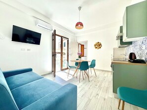 En moderne stue med en blå sofa, et spiseområde med turkise stole, og et køkken med en grøn bordplade.