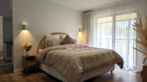 A bedroom with a large bed, two bedside tables with lamps, a nightstand, and a window with sheer curtains. - Luxury Home in Countryside Setting close to Beaches, Bushland, Restaurants/Shops (North Arm)