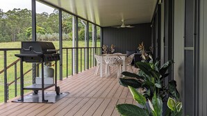 A covered outdoor patio with a grill, a table with chairs, and potted plants. - Luxury Home in Countryside Setting close to Beaches, Bushland, Restaurants/Shops (North Arm)