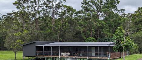A modern house with a large deck, surrounded by a fenced yard and dense forest.