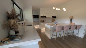 A modern kitchen with a white countertop, gold faucet, and a bar area with pink chairs. - Luxury Home in Countryside Setting close to Beaches, Bushland, Restaurants/Shops (North Arm)