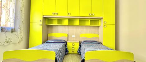 Una habitación con dos camas, armarios amarillo brillante y una ventana con una planta.