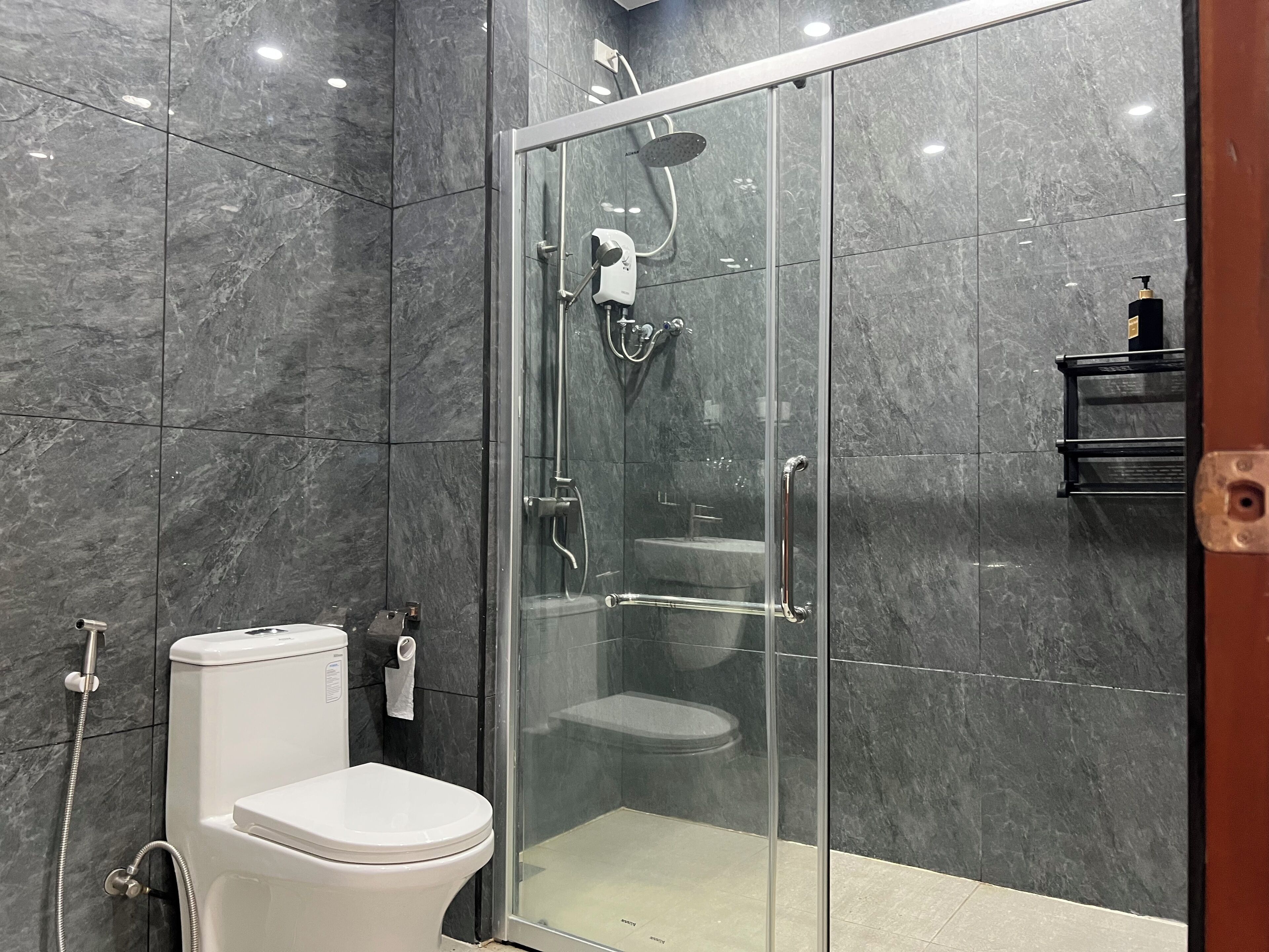 Une salle de bain moderne avec une douche en verre, des toilettes blanches et un mur recouvert de carreaux de marbre.