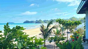 Blick auf einen Strand mit blauem Himmel, Palmen und sandigem Ufer.