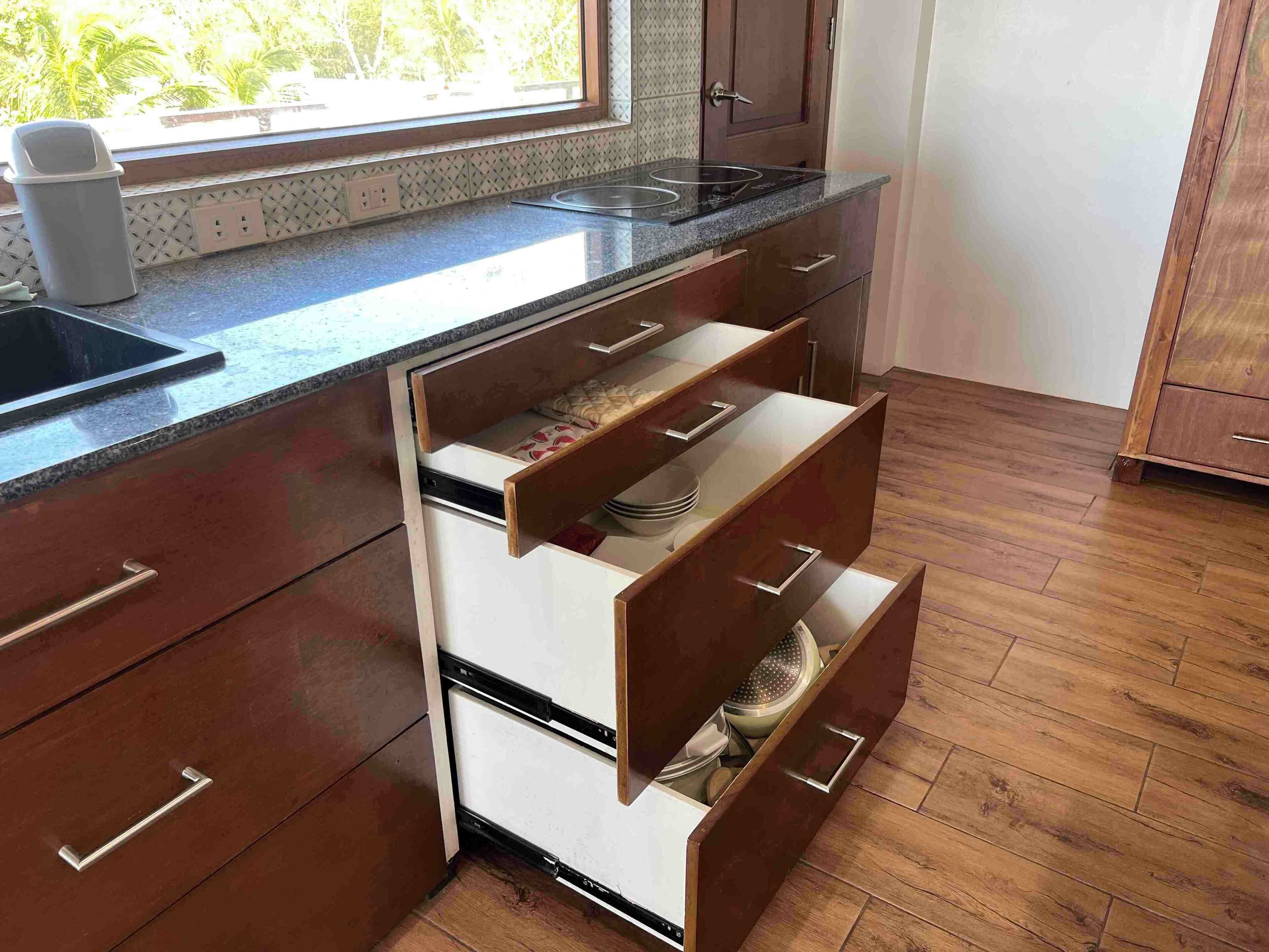 Een keuken met houten kastjes, een inbouwfornuis en een raam met uitzicht op bomen.