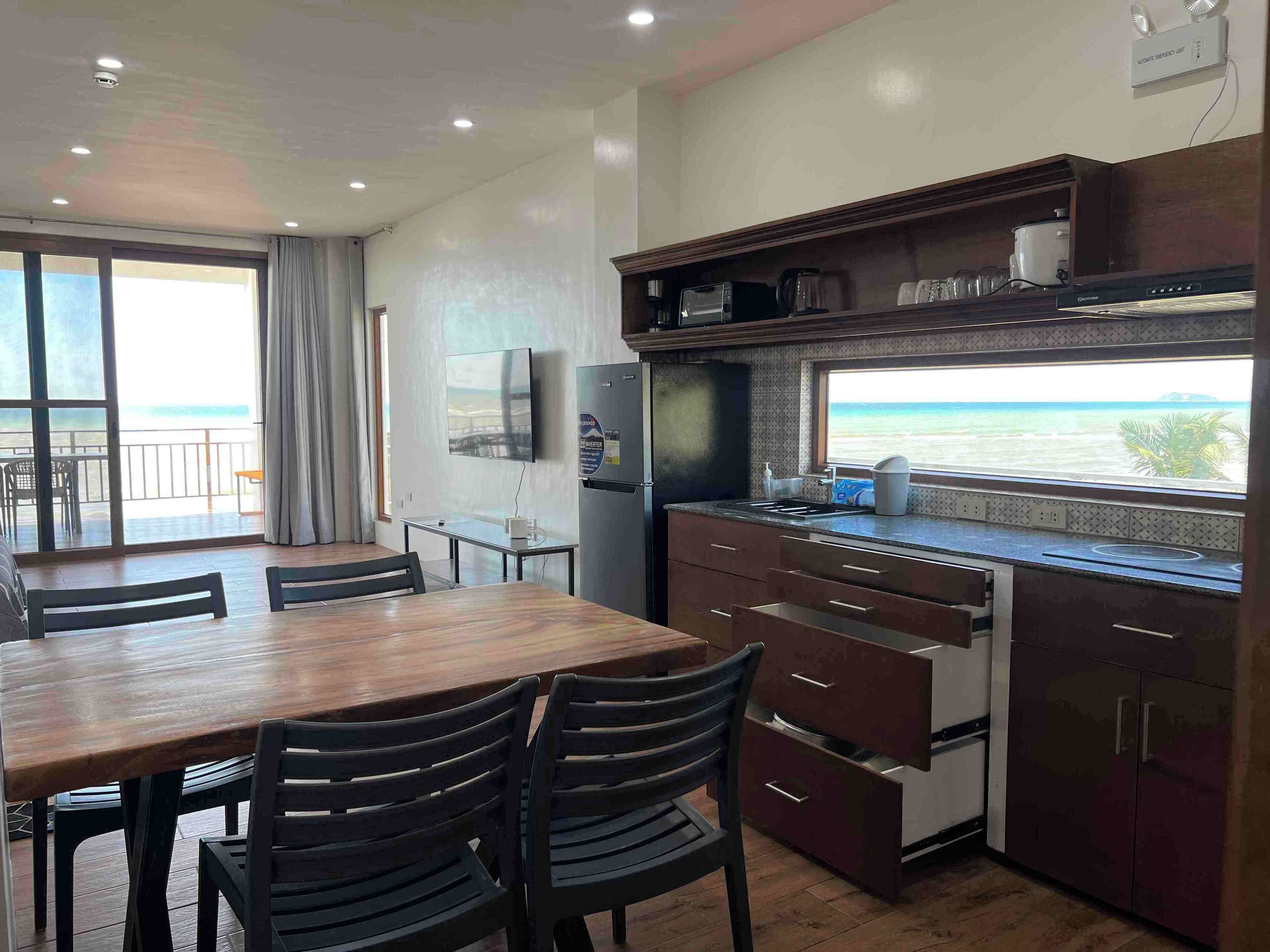 Cocina compacta con comedor, televisor montado en la pared y vista al mar a través de una ventana.