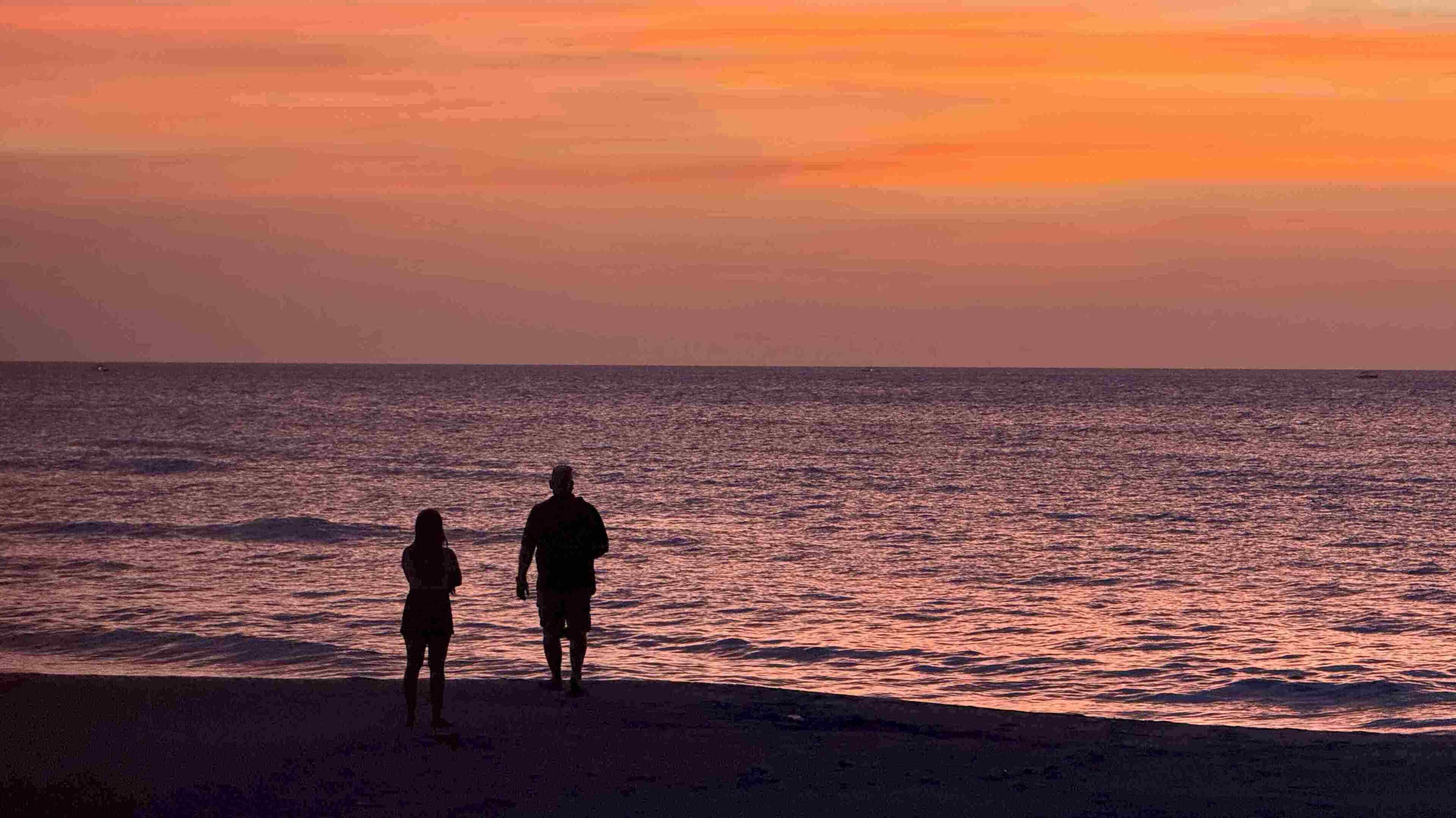 Two people standing on a beach at sunset.