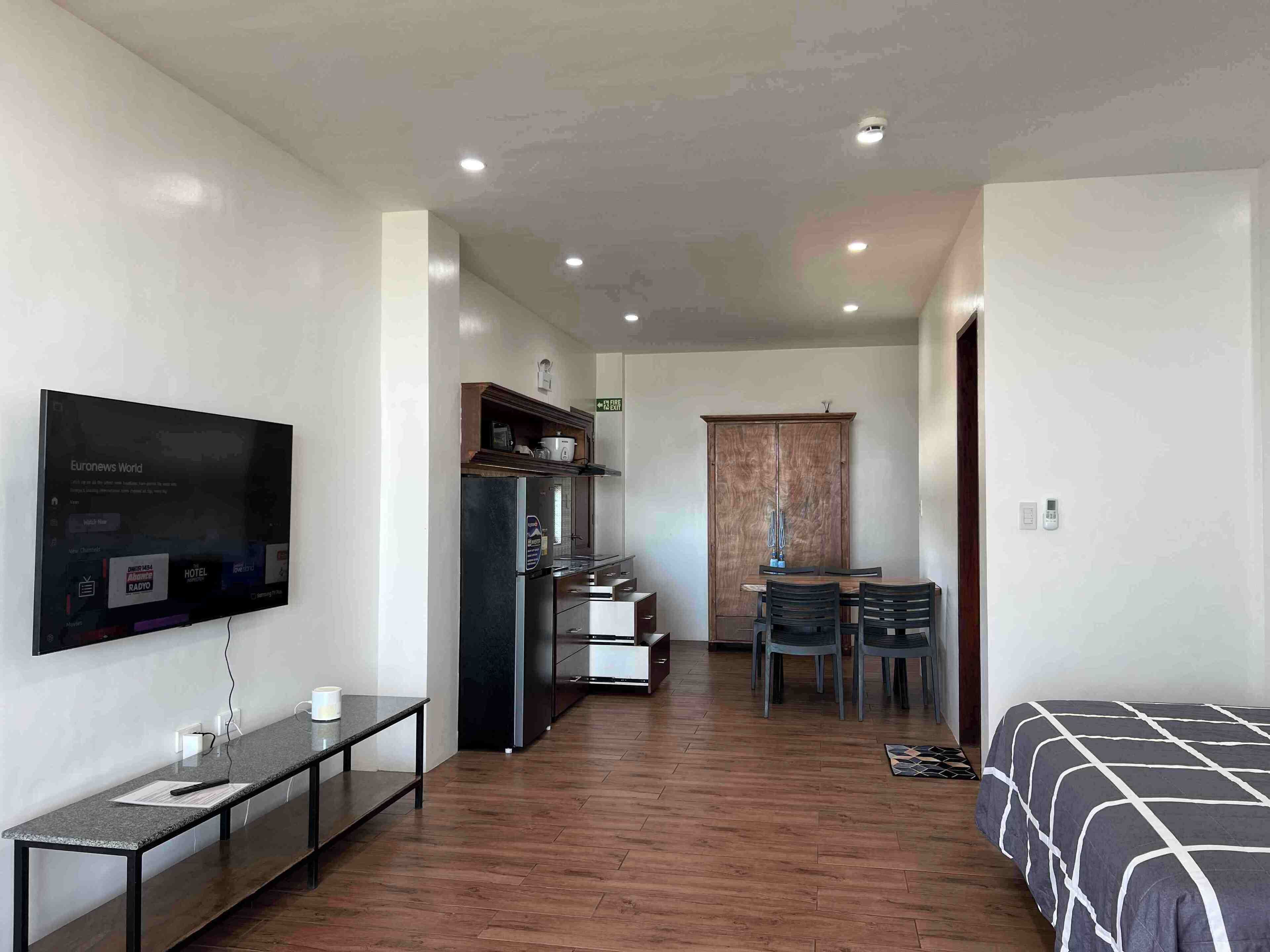 A hotel room with a bed, a desk, a chair, a television, a wardrobe, and a small kitchen area.